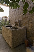 Rustic stone trough with water in front of a natural stone wall and a waterspout