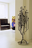 Wrought iron candelabra in front of a wall and view into a living room of an old wooden bench in front of a window