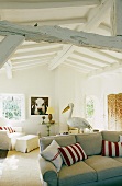 Living room with a sofa and red and white cushions in a converted attic with rustic white wood construction ceiling