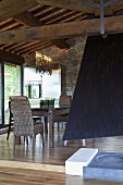 Open fireplace with a black flue and raised dining area under a wooden beam ceiling