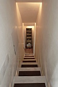 Looking down a narrow stairwell with indirect lighting at a cupboard at the bottom of the stairs