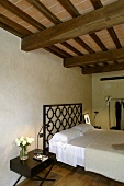 An elegant bedroom beneath a rustic wooden beam ceiling in a renovated country home