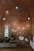 Designer style vanity with improvised lighting made of hanging light bulbs in front of a brick wall and barrel ceiling