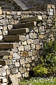 Auskragende Treppenstufen aus Steinblock auf Natursteinmauer