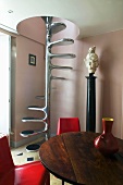Wooden table with red chairs in front of metal spiral staircase with a spindle