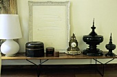 Still life on a wooden table top - white table lamp, a set of brown canisters, Rococo clock and black Asian containers