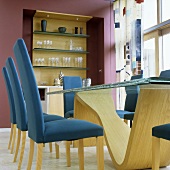 Blue upholstered chairs at a dining table with a curved wooden base and a shelf built into a red wall