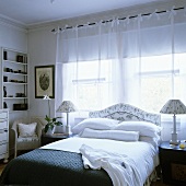 Lichtdurchfluteter Schlafraum mit Doppelbett vor Fenster und leichten Vorhängen