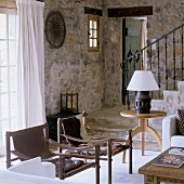 Leather chairs and an occasional table in front of a natural stone wall and a flight of stairs with black metal banisters