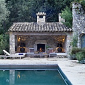 A pool and an open-fronted Mediterranean-style building with atmospheric lighting in front of a natural stone wall and a fireplace