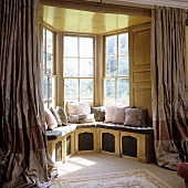 Open curtains in front of a bay window with a view and a built-in window seat with pink cushions