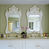 A marble table top with two wash basins and white-framed mirrors on a grey-painted wall