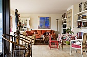 A living room with old wooden chairs and a colourful dining corner against a shelf wall and rustic floor boards