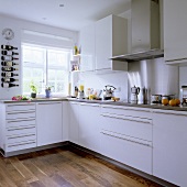A corner of a white fitted kitchen with stainless steel handles and an integrated extractor hood