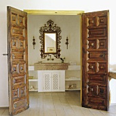 Open carved wooden doors with a view of a stone basin with a mirror in a gold frame