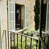 A view over a leafy courtyard onto a window with light green shutters and black railings