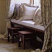 Cushions with white-grey covers on a built-in window seat with dark wooden stools