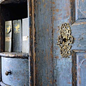 Detail of a piece of old wooden furniture with blue paint and a lock with a decorative frame and a key
