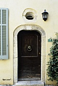 A dark wooden front door with a stone frame and a window above in the light yellow facade