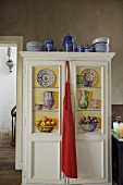 Blue crockery on a painted kitchen cupboard with a red apron hanging from the door