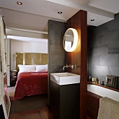 A bedroom with an en-suite bathroom - a wash basin with wall lighting in a partition wall with a view of the bed