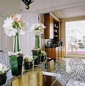 White amaryllis in a glass vase on a glass table with open swing doors and view of a fitted kitchen