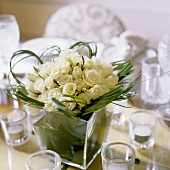 A bunch of white roses and decorative grass in a glass vase surrounded by tea lights