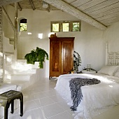 A cool white bedroom in a tropical holiday home with an antique wooden cupboard and a flight of stairs