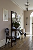 An elegant hallway with dark antique chairs, a wall table and old floor boards