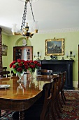 Wooden table and chandelier in front of a fireplace in an elegant dining room with green walls