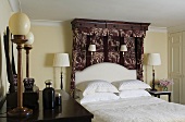 An English bedroom with table and wall lamps, a double bed with a patterned canopy and white bedclothes