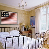 Bett mit Metallgestell vor gelbgetönter Wand mit stilisierter amerikanischer Flagge