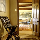 A yellow anteroom with an antique chair and an open door with a view of a grey armchair with an upholstered footstool