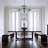 A dining table with a wooden frame and benches with leather cushions in an elegant living room with an art deco-style ceiling lamp