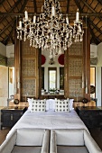 A chandelier and a double bed in front of a room divider with a view into a bedroom in a South African house
