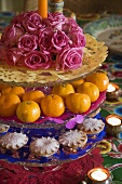 A cake stand with roses, mandarins, cakes and tea lights