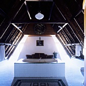 Bad im südafrikanischen Landhaus - weiße Badewanne in Raummitte unter Dachstuhl mit dramatischer Lichtinszenierung