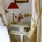 A bedside lamp with a red shade and a glass candlestick on a Rococo-style table