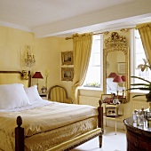 Eleganter Schlafraum mit antikem Bett und Spiegel im Goldrahmen an gelb getönter Wand