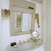 A marble-topped washstand and a vintage mirror with a grey frame in the corner of a bathroom