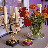 Red flowers in a glass vase and a gilded candle stick next to a mocca cup on a wooden shelf