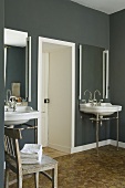 Clean lines in a bathroom - wash basins with mirrors and vertical strip lighting on a grey wall either side of the door