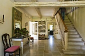 An entrance hall with a natural stone floor and a flight of stairs with a rustic wood beam ceiling
