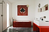 A minimalistic bathroom - a wash basin on a red table and a red glass bathtub on a concrete floor