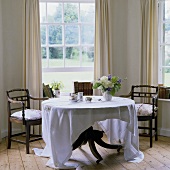 A dining table with dark wooden chairs in a bay window with a view of a garden