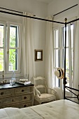 A vintage-style chest of drawers and a chair in the corner of a bedroom with a view