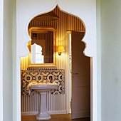 A view through an Oriental pointed archway onto a wash basin with an ornamental foot and a mirror above