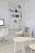 weiße Raumecke mit Hockergruppe und Designerstühle vor Arbeitszeile mit Wandregal