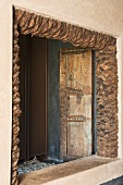 An unglazed window with a rustic natural stone frame and a view if an old door