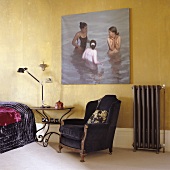 An antique armchair and a side table in front of a gold-painted wall hung with a painting